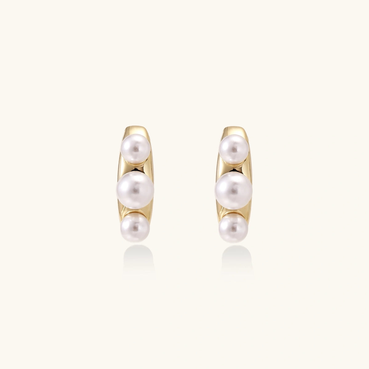 14K gold-plated curved stud earrings with three white freshwater pearls aligned vertically on cream background
