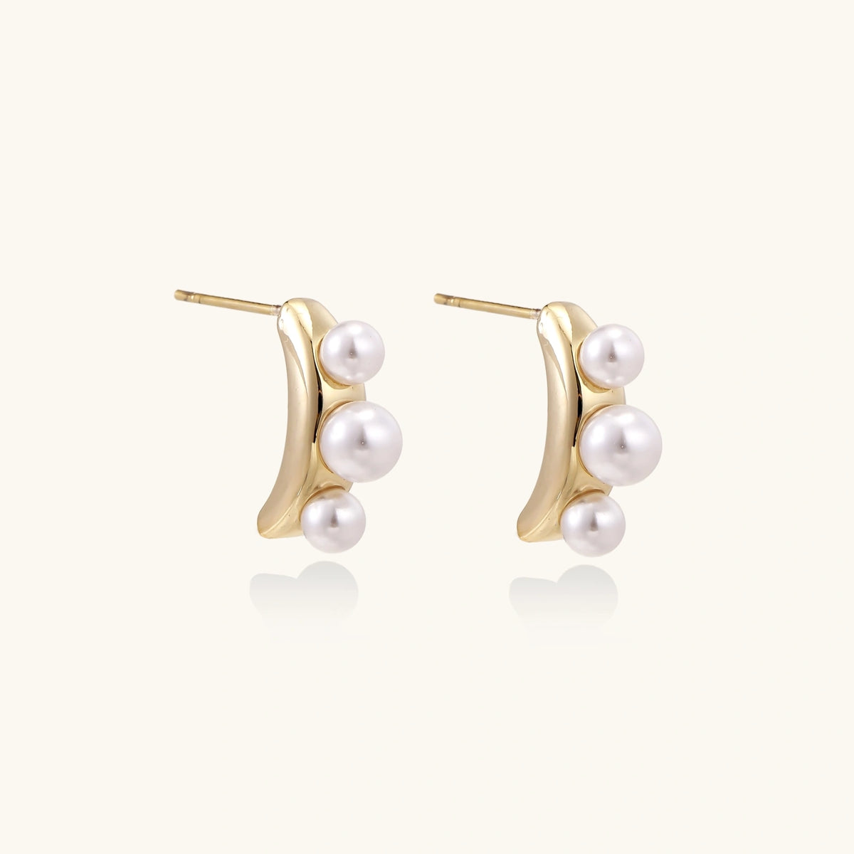 14K gold-plated curved stud earrings with three white freshwater pearls aligned vertically on cream background